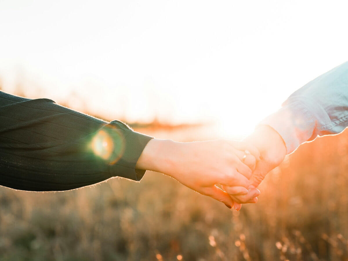 Stabile Beziehungen & Partnerschaft Ein Paar hält sich an den Händen, von warmem Licht beschienen, als Symbol für stabile und erfüllende Beziehungen.